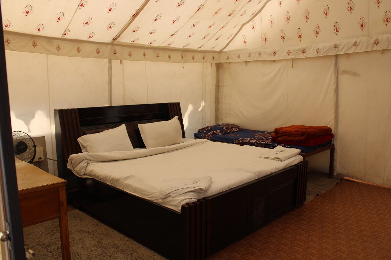 Ein Zeltraum mit Bett, kleinem Tisch und Ventilator.