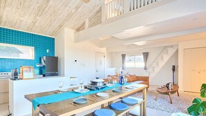 A spacious kitchen with a wooden ceiling, a dining area with a long table set for four, and a staircase leading to an upper level.