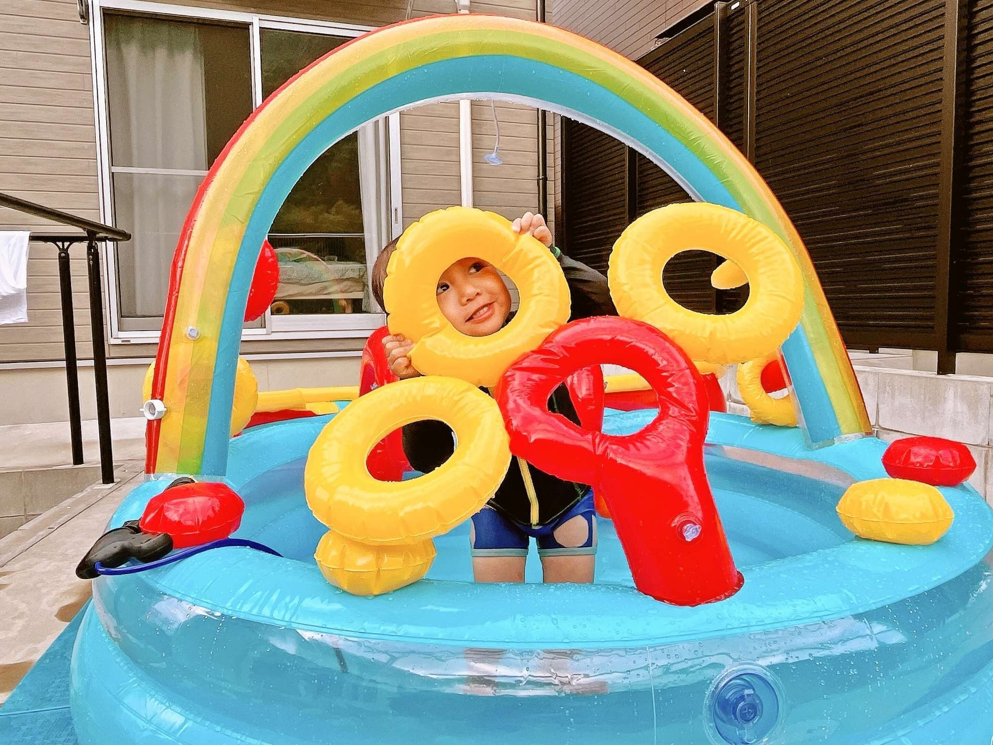 A child in a blue inflatable pool with a rainbow arch and yellow and red rings.