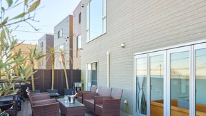 A deck with wicker furniture, a glass table, and a sliding glass door leading to a wooden deck.