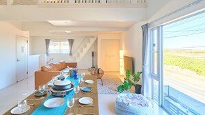 A modern dining area with a long table set for a meal, a sofa, and a large window with a view.