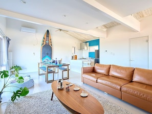 A modern living room with a brown leather sofa, a wooden coffee table, and a dining area with a table set for four.