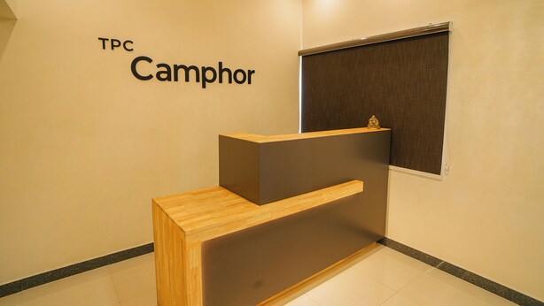 Een receptiebalie met een houten, donker paneelontwerp, een bord met de tekst 'TPC Camphor' en een raam met een zonwering.