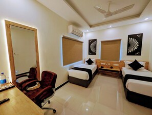 A hotel room with two beds, a desk with a chair, an air conditioner, and artwork on the walls. - TPC Camphor (Tiruchirappalli)