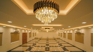 Een ruime hotellobby met een grote kroonluchter, een schaakbordvloer en een lange gang met deuren aan één kant.