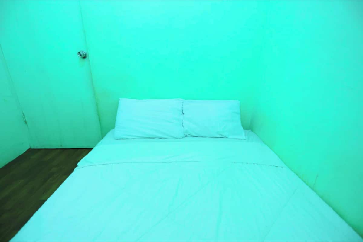 A small, single-bed room with a wooden floor and plain walls.