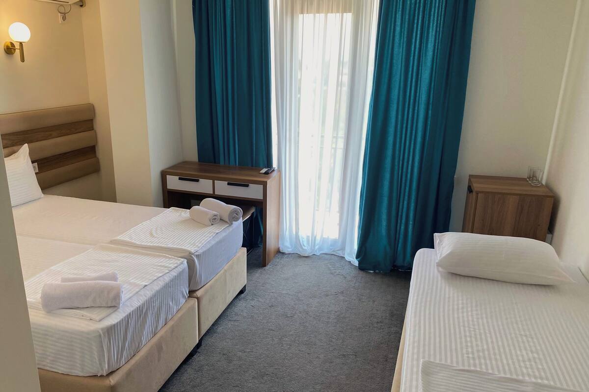 A hotel room with two beds, a wooden nightstand, a small table, and a wall-mounted lamp.