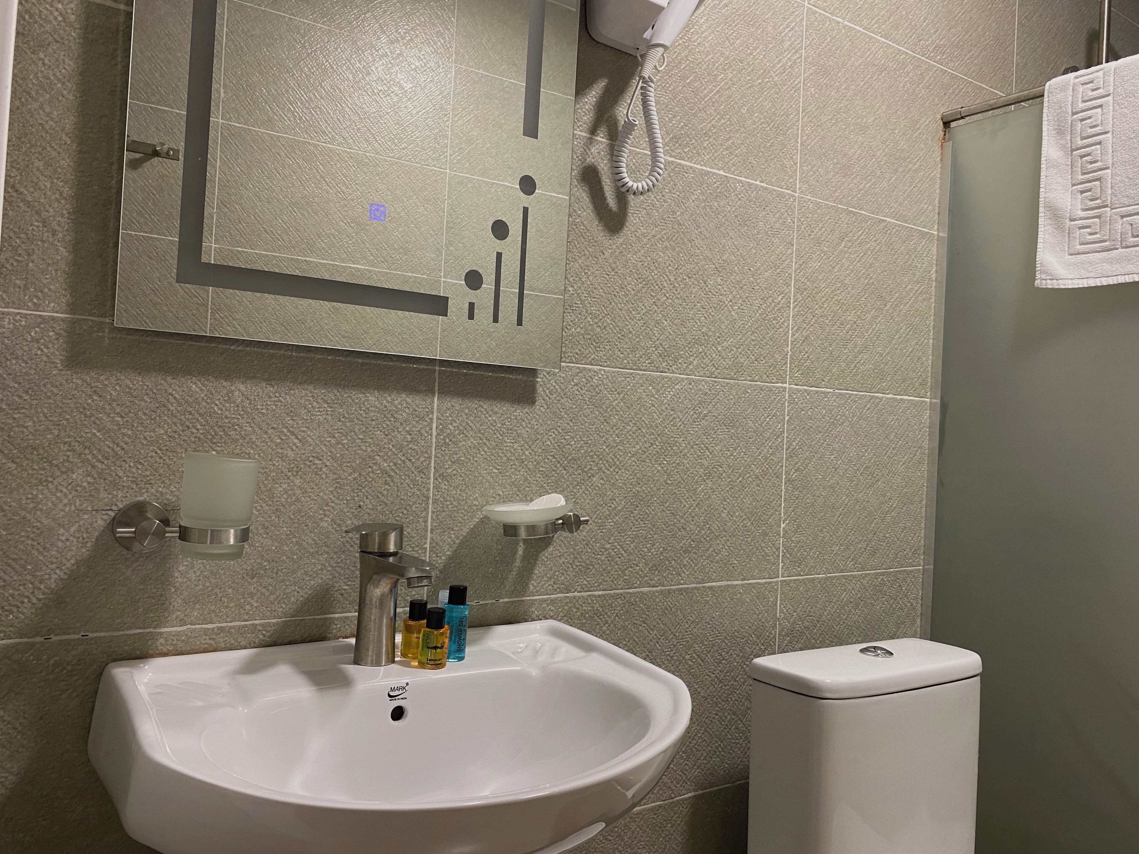 A bathroom with a white sink, a toilet, and a mirror above the sink. There are three bottles of liquid soap on the sink.