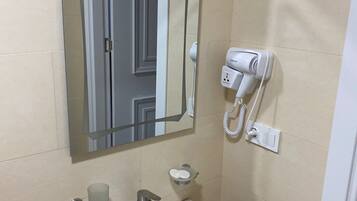 Un baño con lavamanos blanco, un espejo, secador de pelo y jabonera.