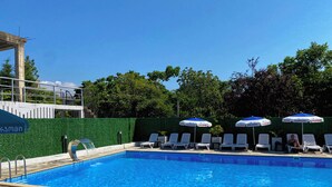 Ein Schwimmbecken mit Liegestühlen und Sonnenschirmen, umgeben von Grünpflanzen.