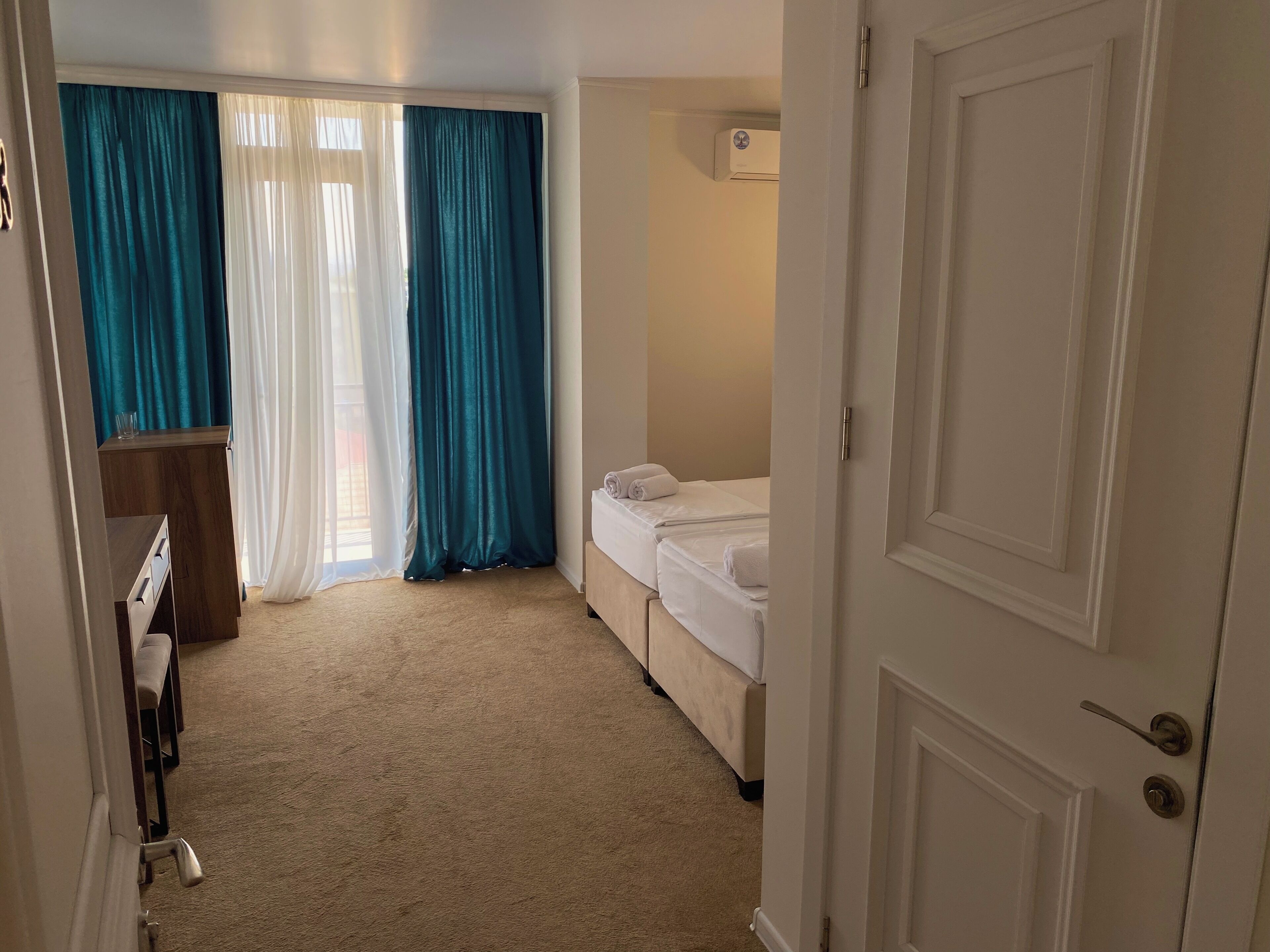 Et hotelværelse med seng, skrivebord og et vindue med gardiner.