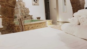 A hotel room with a bed, a small bathroom with a sink, and a stone wall. - Janara - Arch of Trajan (BENEVENTO)