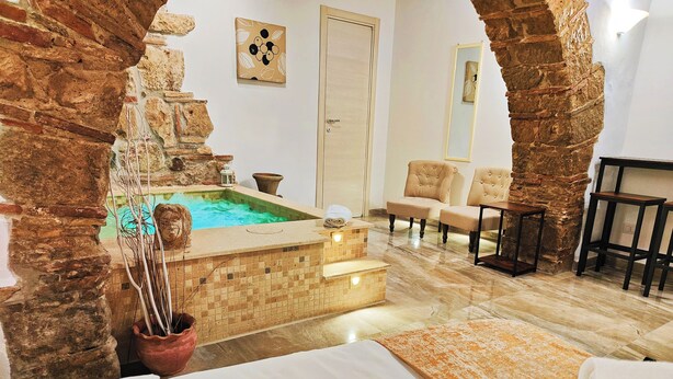 A spa room with a stone wall, a small pool, a massage table, and two chairs. - Janara - Arch of Trajan (BENEVENTO)