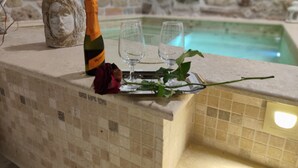 A stone wall with a pool, a bottle of champagne, and two glasses on a tiled counter. - Janara - Arch of Trajan (BENEVENTO)