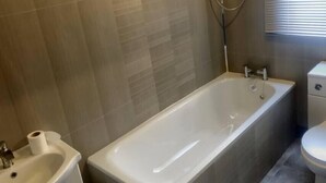Et badeværelse med badekar, vask og toilet.