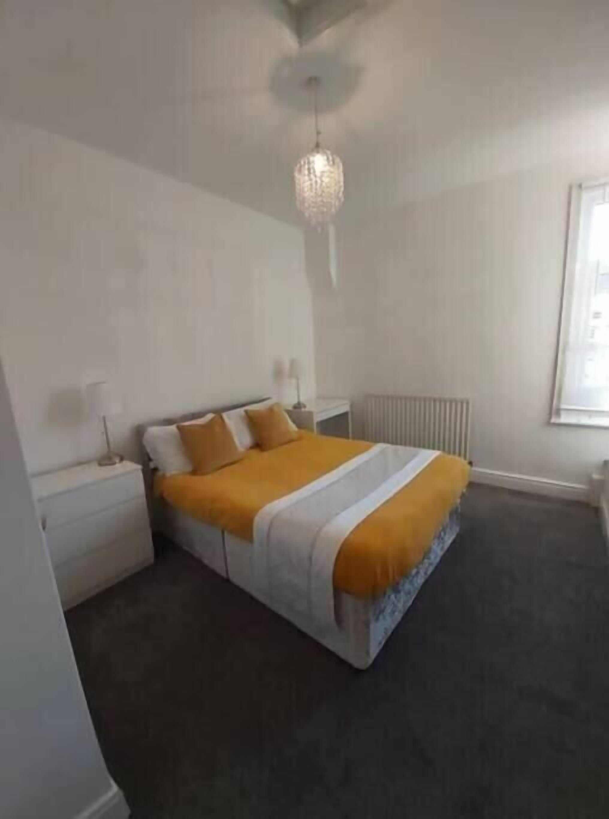 A bedroom with a bed, nightstands, a radiator, and a window.