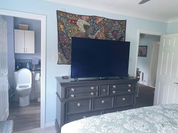 A bedroom with a bed, a dresser, a television, a tapestry, and a bathroom visible through an open door. - Comfortable family home adjacent to Millfield School and near Clarks Village (Street)