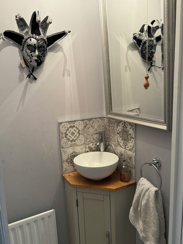 A bathroom with a white sink, a mirror, and a decorative mask on the wall. - Comfortable family home adjacent to Millfield School and near Clarks Village (Street)