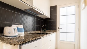 A compact kitchen with a granite countertop, a coffee maker, a kettle, and a sink. - Las Casitas de Corralejo (La Oliva)
