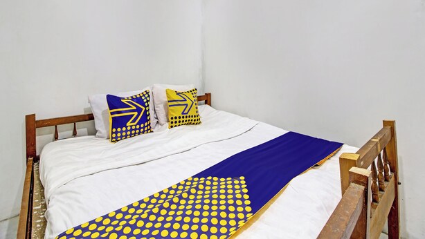 A bed with a white sheet, two pillows with blue and yellow patterns, and a blue and yellow blanket. - Hotel O Luqman Kostel Syariah (Semarang)