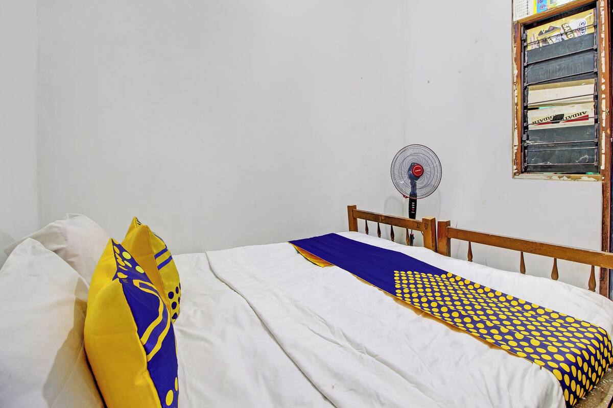 A bedroom with a single bed, a wooden headboard, a wall-mounted fan, and a window with a calendar.