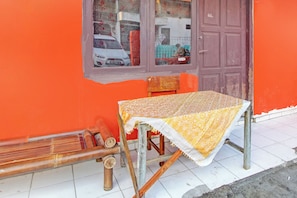 A table with a patterned tablecloth, a chair, and a window with a view of a parked car and a building in the background. - Hotel O Luqman Kostel Syariah (Semarang)