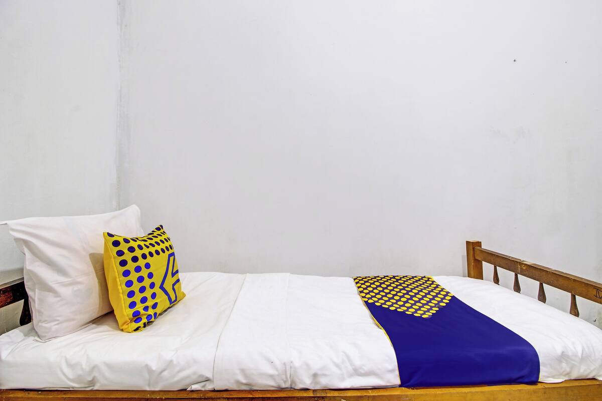 A single bed with white bedding, a yellow pillow with blue dots, and a blue blanket with yellow dots.