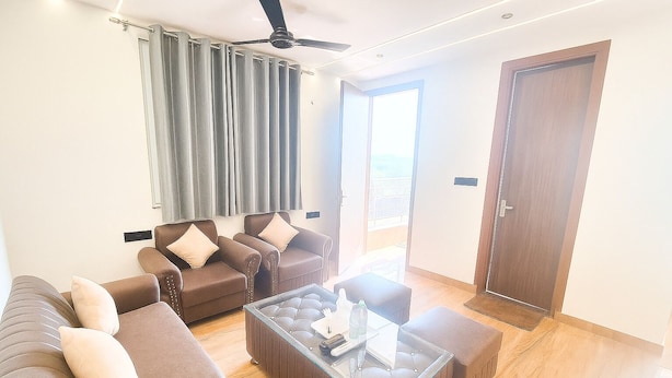 A modern living room with a sofa, two armchairs, a glass coffee table, and a ceiling fan. - DIPLOMAT REGENCY (New Delhi)