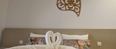 A neatly made bed with a heart-shaped towel arrangement and a decorative wall piece.