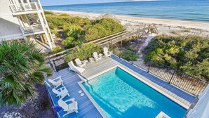 A pool with a wooden deck and lounge chairs, surrounded by greenery and a beach view. - Welcome to Beachfront Benefits! (St. George Island)