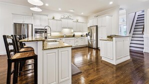 A spacious kitchen with white cabinets, stainless steel appliances, and a wooden dining area. - Welcome to Sandy Bottoms! (St. George Island)