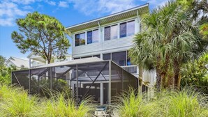 A two-story house with a covered patio area, surrounded by tall grasses and trees. - Welcome to Sandy Bottoms! (St. George Island)