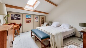 Un dormitorio con cama, banco, escritorio, silla y obras de arte en las paredes.