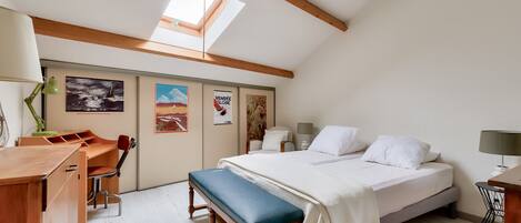 Un dormitorio con cama, banco, escritorio, silla y obras de arte en las paredes.