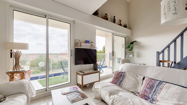 Amplia sala de estar con un sofá blanco, una mesa de centro y un televisor. Hay un balcón con vistas al jardín.