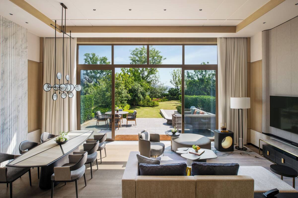 A modern living room with a dining area, large windows, and a TV.