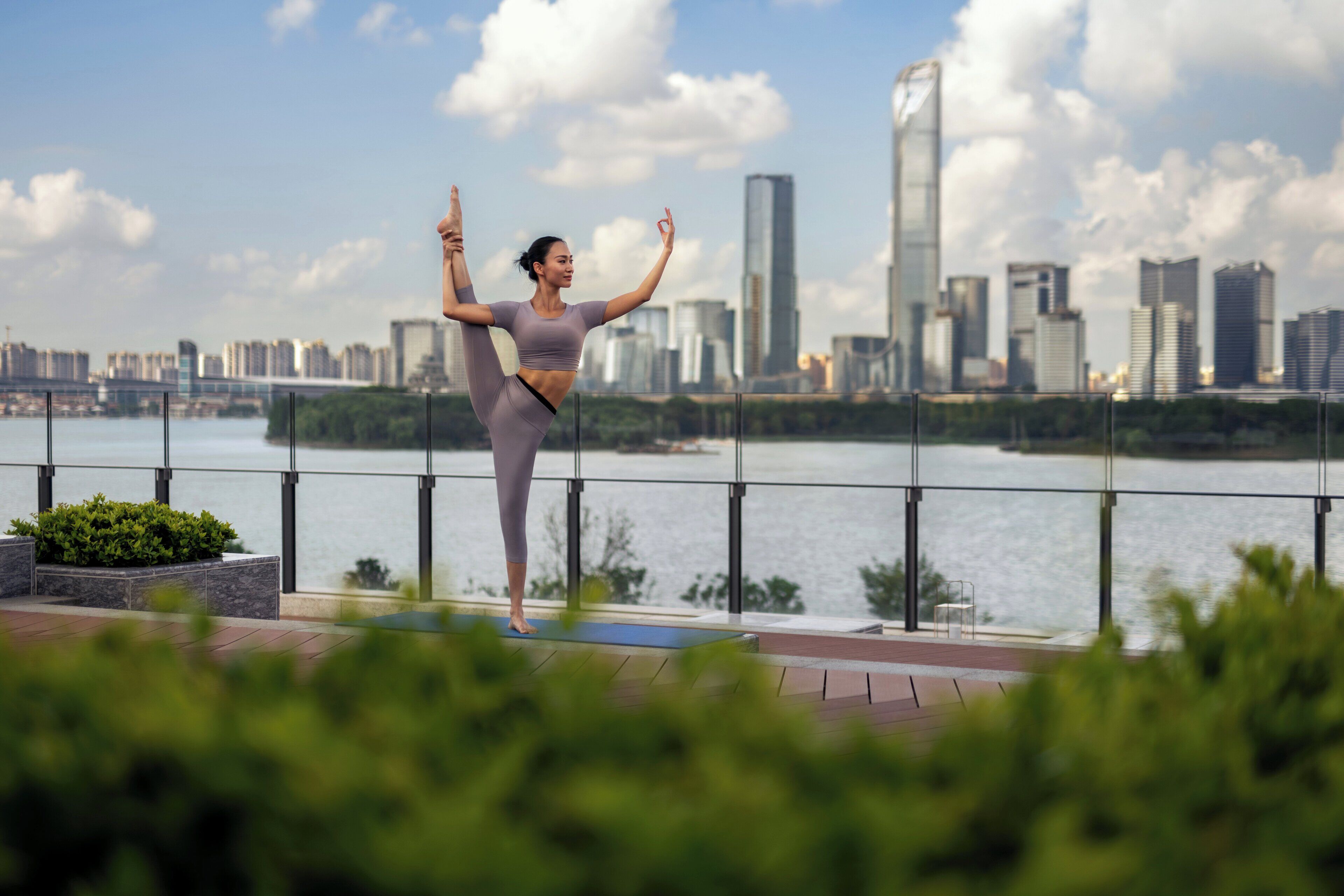 Une personne effectuant une posture de yoga sur un balcon, avec une vue sur la ville en arrière-plan.