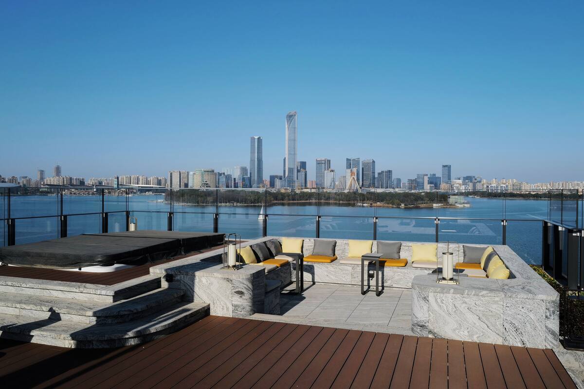 A rooftop terrace with seating and a view of a city skyline across a body of water.