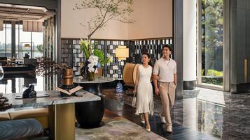 Un vestíbulo moderno con una recepción de mármol, un jarrón grande con flores y una zona de estar con un banco.