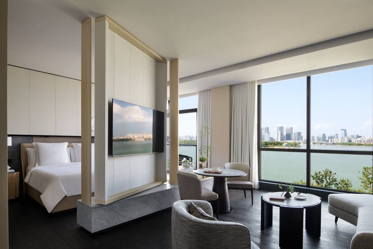 A modern hotel room with a bed, seating area, and a large window offering a city view.