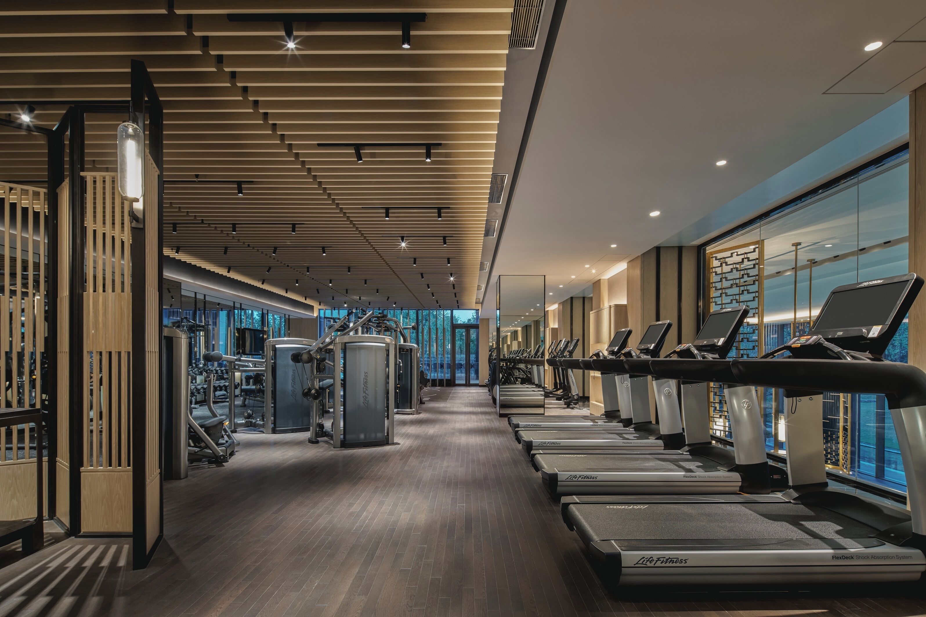 A gym with treadmills, weight machines, and a wooden floor.