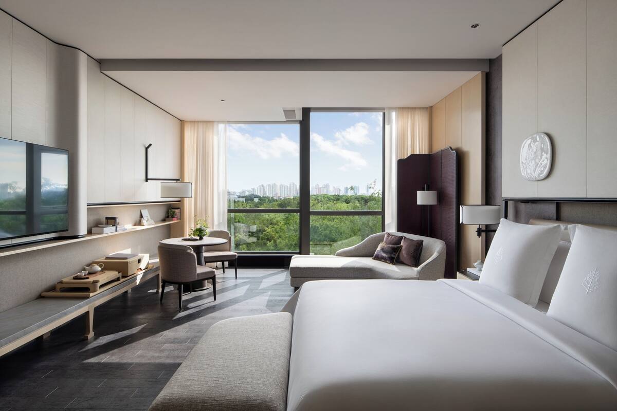 A modern hotel room with a large bed, a desk, a chair, and a TV.