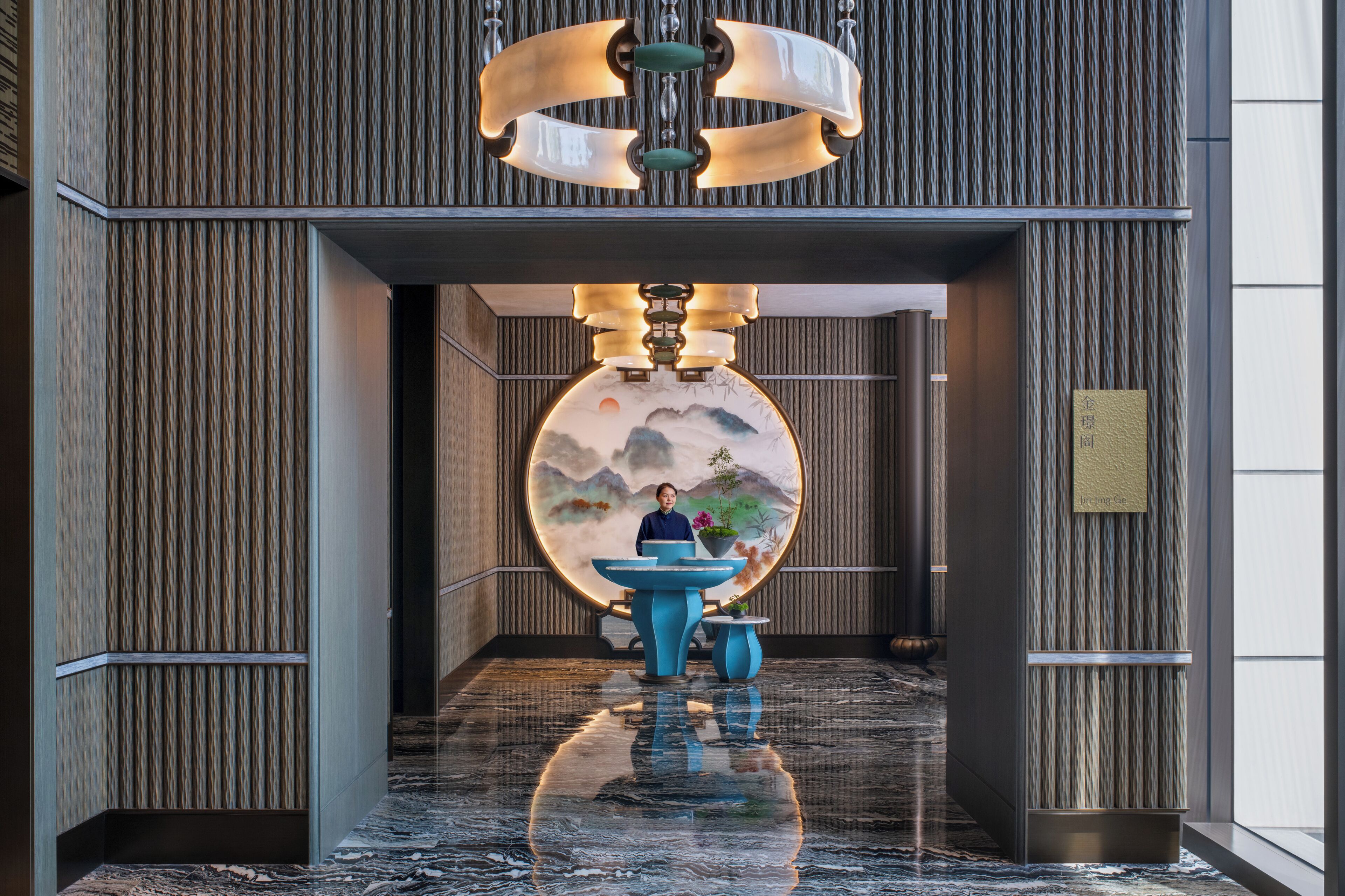 A modern lobby with a large circular mural, a fountain, and a person standing near the entrance.