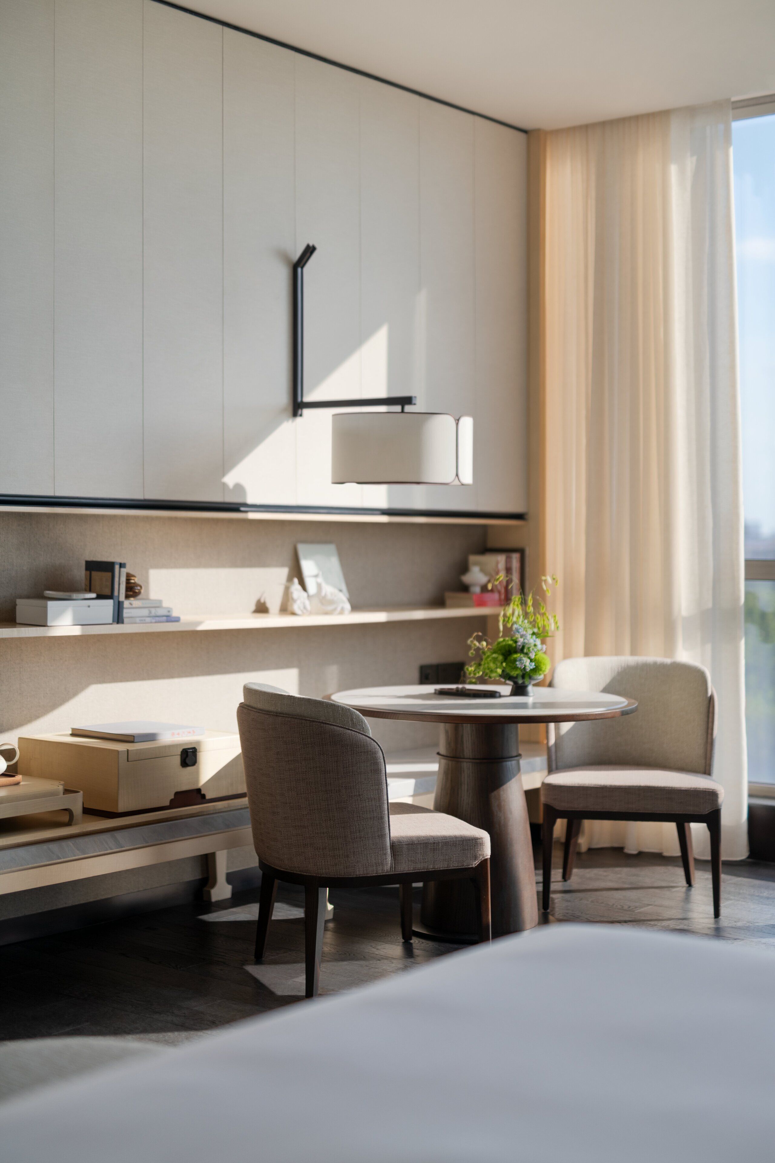 Una habitación de hotel moderna con diseño minimalista, que incluye un comedor con dos sillas, una mesita redonda y una cocina integrada con armarios y encimera.