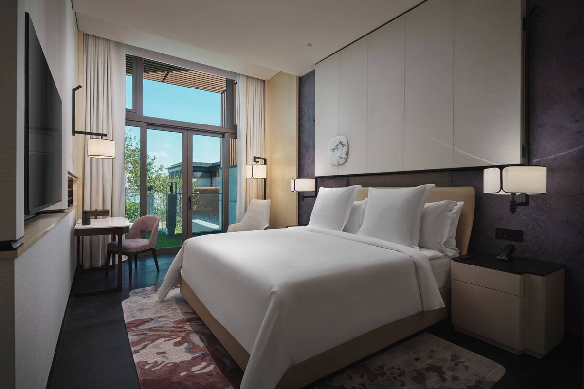 A modern hotel room with a large bed, bedside tables, a desk with a chair, and a TV.