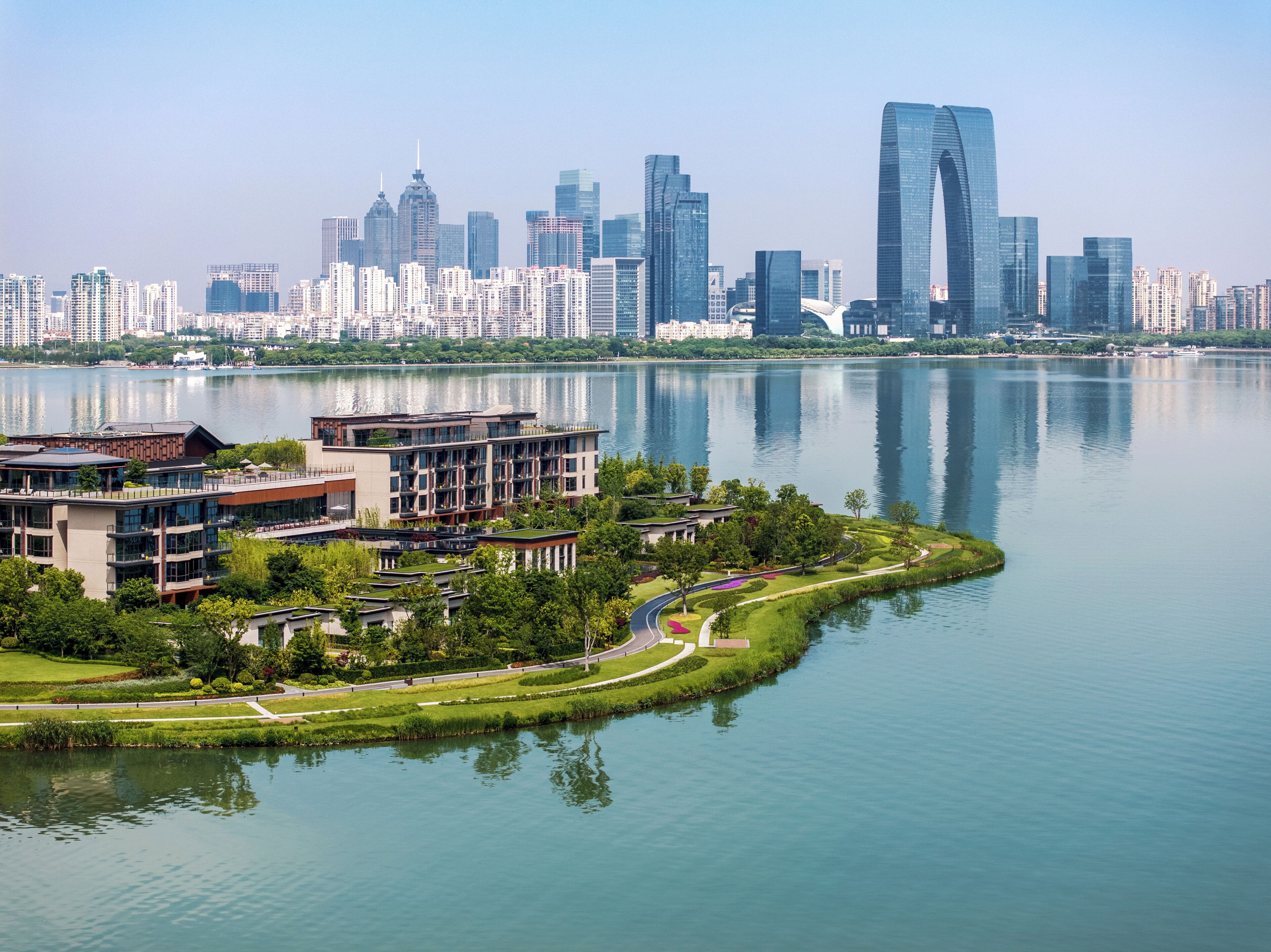 A modern building complex with a waterfront view, surrounded by greenery and a calm lake.