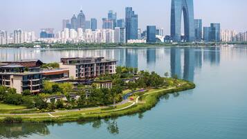 A modern building complex with a waterfront view, surrounded by greenery and a calm lake.