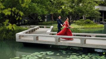 A couple walking on a stone bridge over a pond with lily pads.