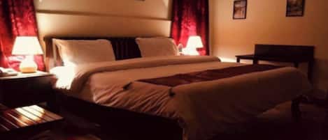 Une chambre d’hôtel avec un lit, une table de chevet, une lampe et un banc en bois.