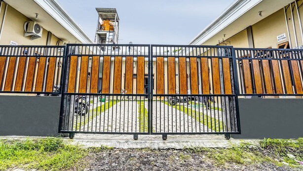 A gated entrance with a wooden fence and a black metal gate. - OYO 92541 Suny Kost Syariah (Sidoarjo)